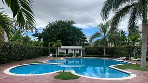 A swimming pool with a unique design, surrounded by palm trees and a small building in the background.