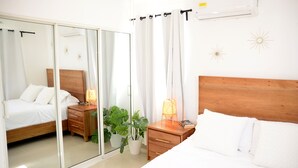 A bedroom with a wooden headboard, a bedside table with a lamp, a mirror, and a potted plant.
