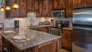 Une cuisine dotée de meubles en bois, de plans de travail en granit, d’appareils électroménagers en acier inoxydable et de luminaires suspendus.