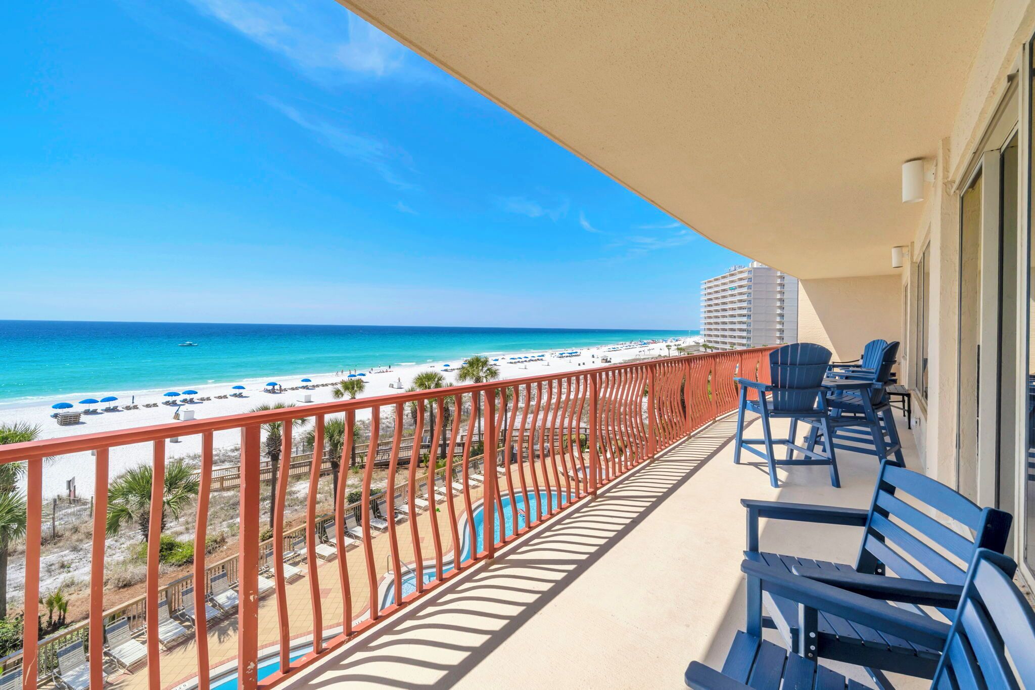 A balcony with a view of the beach, pool, and hotel buildings.
