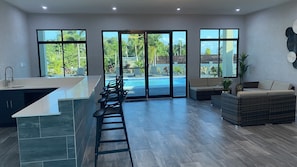 A modern kitchen with a large island, bar stools, and a view of a swimming pool and outdoor area.