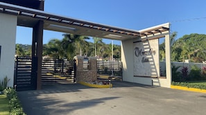 A gated entrance with a pergola, a sign reading "Happy Cove Estate," and a landscaped area with palm trees.