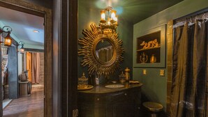 Een badkamer met een grote, versierde spiegel, een wastafelmeubel met een wastafel, en een douchegordijn.