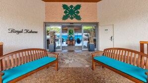 Un hall d’entrée avec deux bancs en bois dotés de coussins turquoise, un grand logo vert sur le mur et une enseigne indiquant « Royal Kahana ».