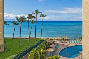 A resort pool area with a view of the ocean, palm trees, and lounge chairs.