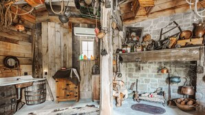 Una stanza rustica con pareti in legno, un camino in pietra e diversi oggetti da cucina d'epoca.