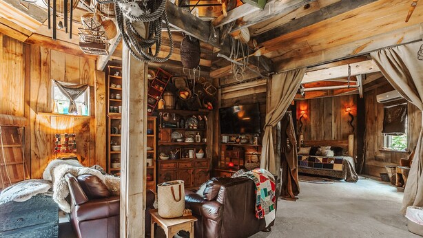 L'interno accogliente di una baita, con un divano in pelle, un tavolo in legno e una libreria piena di oggetti diversi.