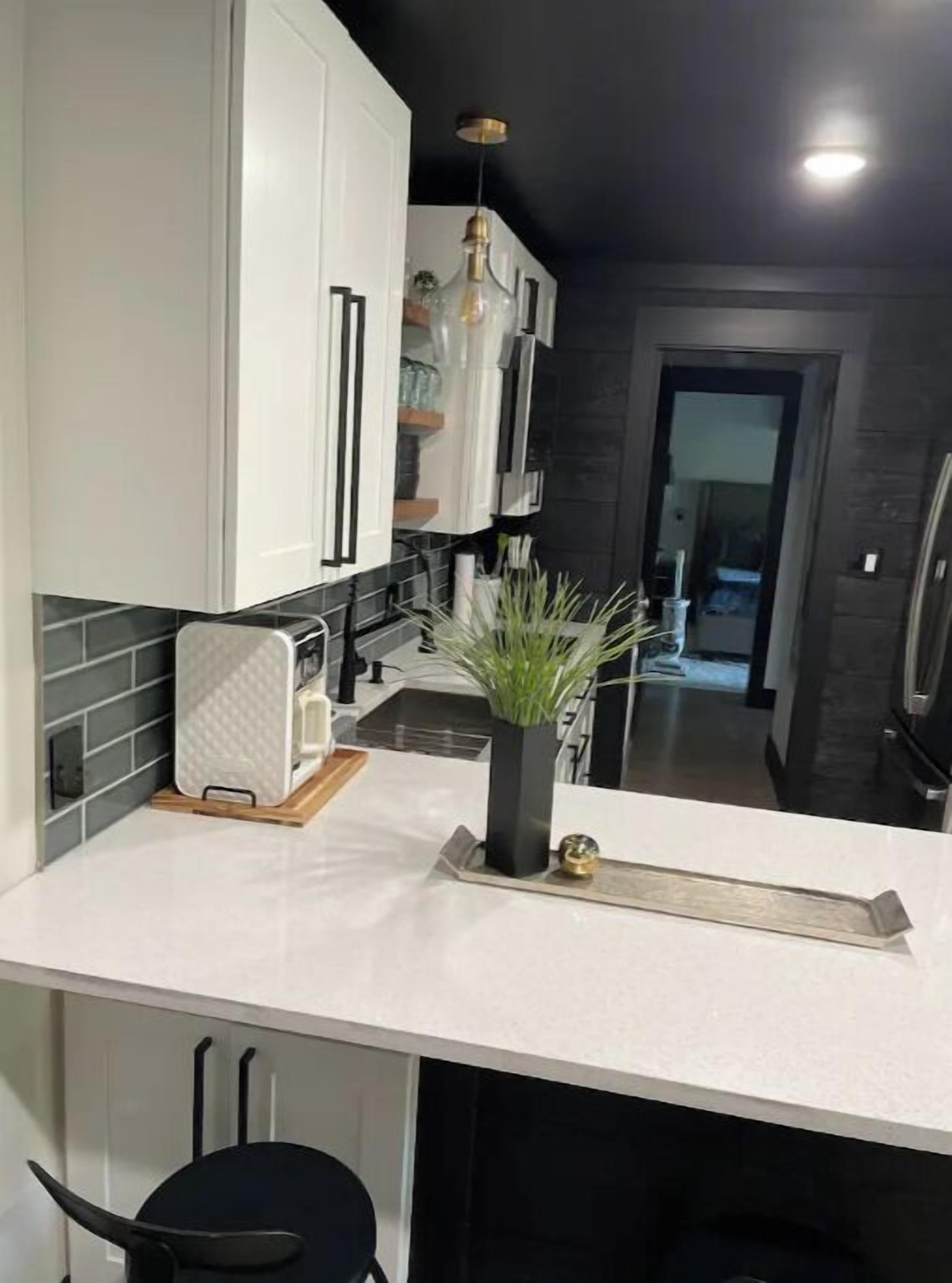 A modern kitchen with white cabinets, a black countertop, and a hanging light fixture.