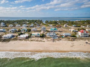 Une zone résidentielle côtière avec des propriétés donnant sur la plage, une jetée s’avançant dans l’eau et un ciel dégagé.