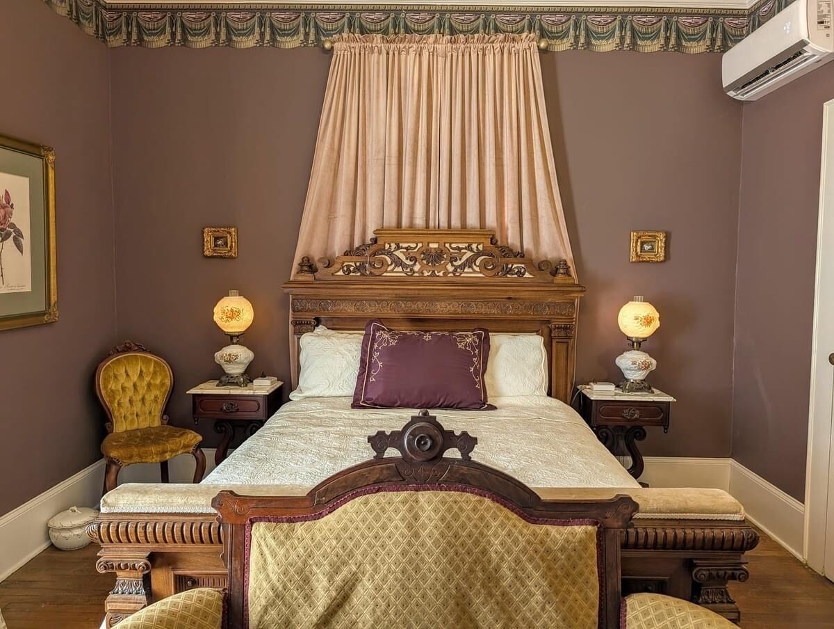 Een klassieke slaapkamer met een groot bed, een versierd hoofdbord en twee nachtkastjes met lampen.