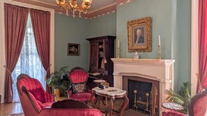 A traditional living room with a fireplace, red upholstered chairs, a chandelier, and a portrait on the wall. - Private Historic House, in Downtown Bristol Virginia! (Bristol)