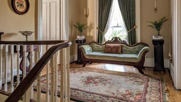 A room with a wooden staircase, a green sofa with a floral cushion, a patterned rug, and two potted plants. - Private Historic House, in Downtown Bristol Virginia! (Bristol)