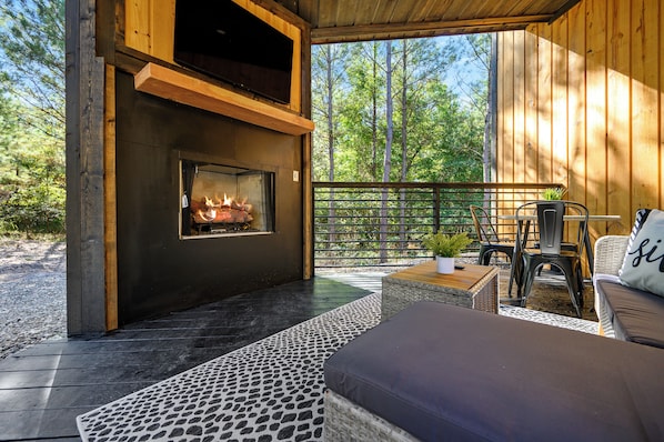Un espace extérieur accueillant avec un foyer, une terrasse en bois et une vue sur la forêt.