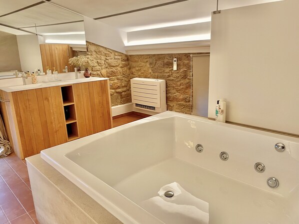 A modern bathroom with a large bathtub, wooden vanity, and a stone wall.