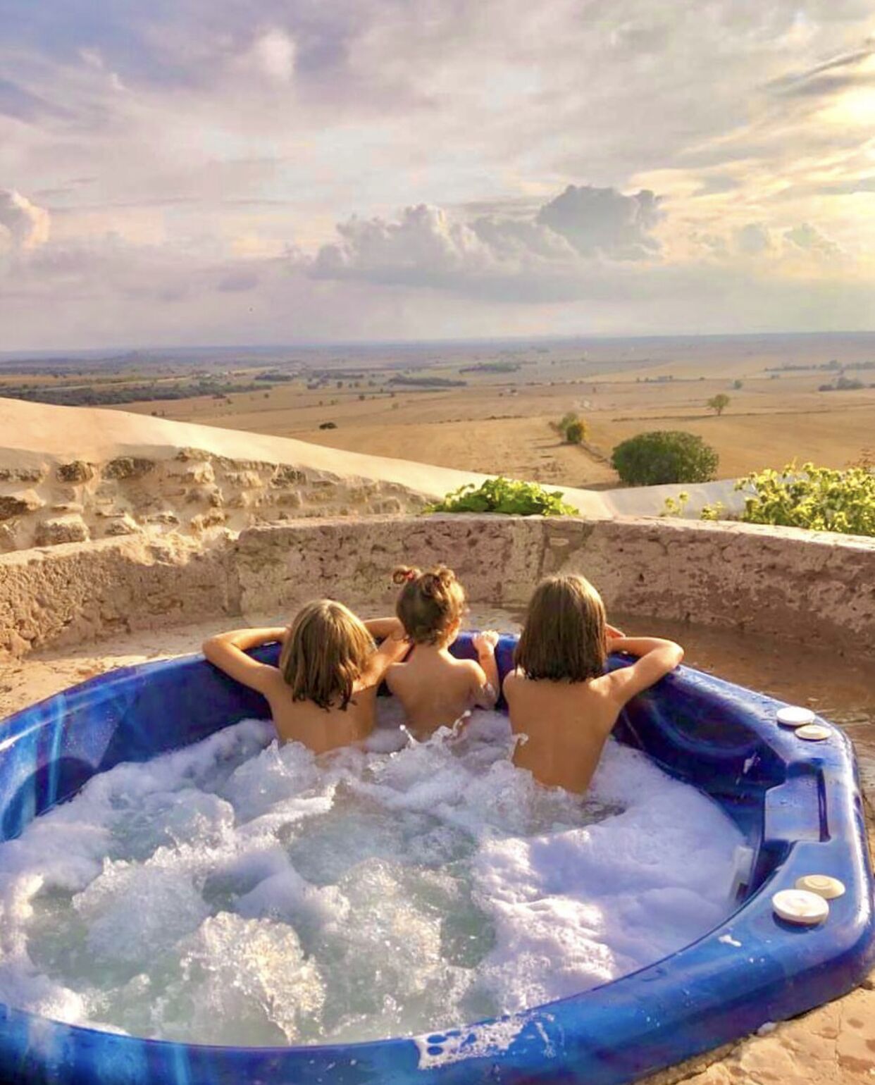Three people relaxing in a blue hot tub with a scenic view of a desert landscape.