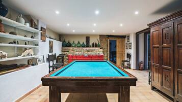 Una mesa de billar en una habitación con estanterías a la izquierda y un mueble de madera a la derecha.