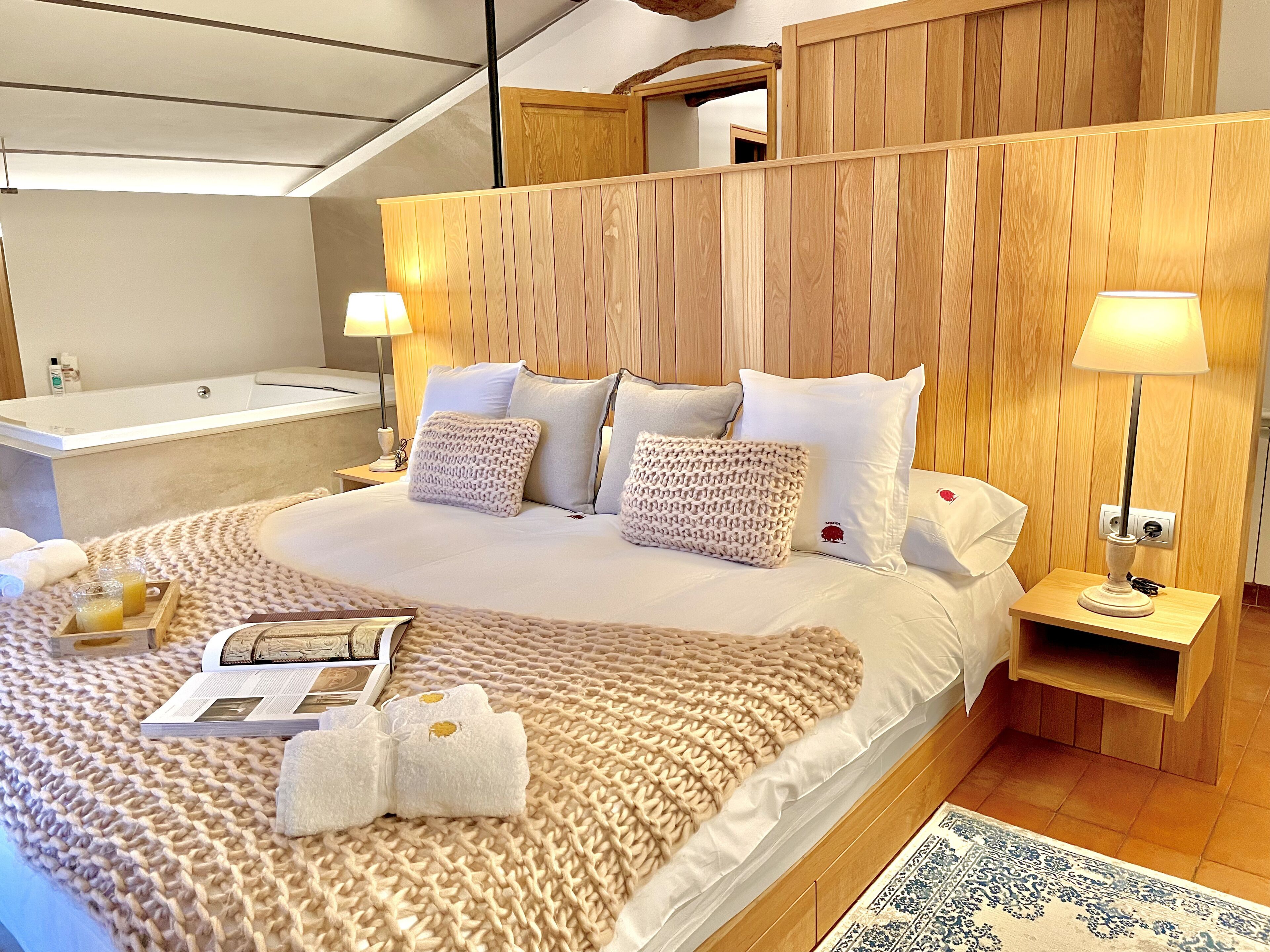 Een netjes opgemaakt bed met een gebreide deken, een houten hoofdbord en twee bedlampjes.