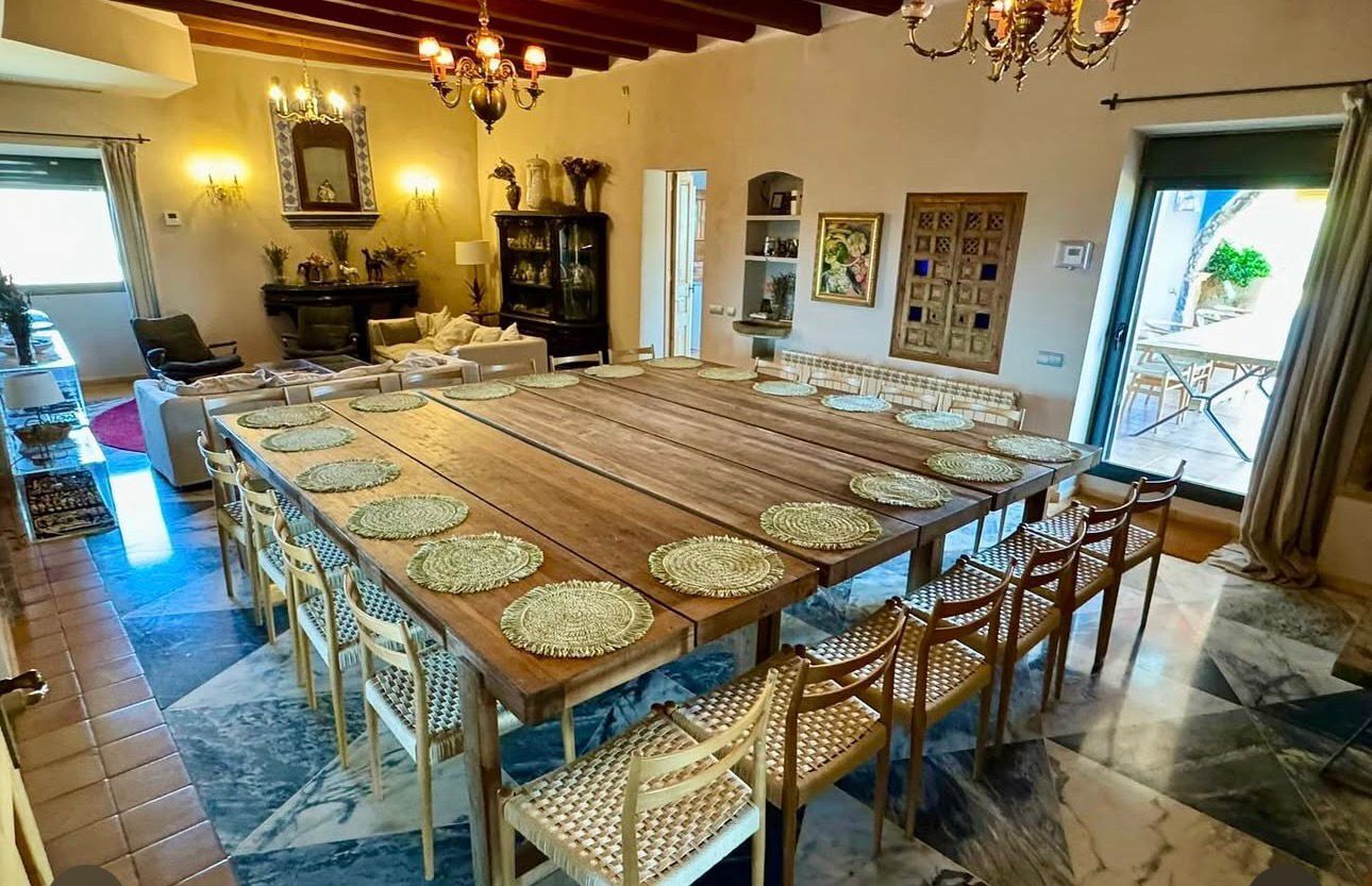 A spacious dining area with a long wooden table, woven placemats, and wicker chairs.