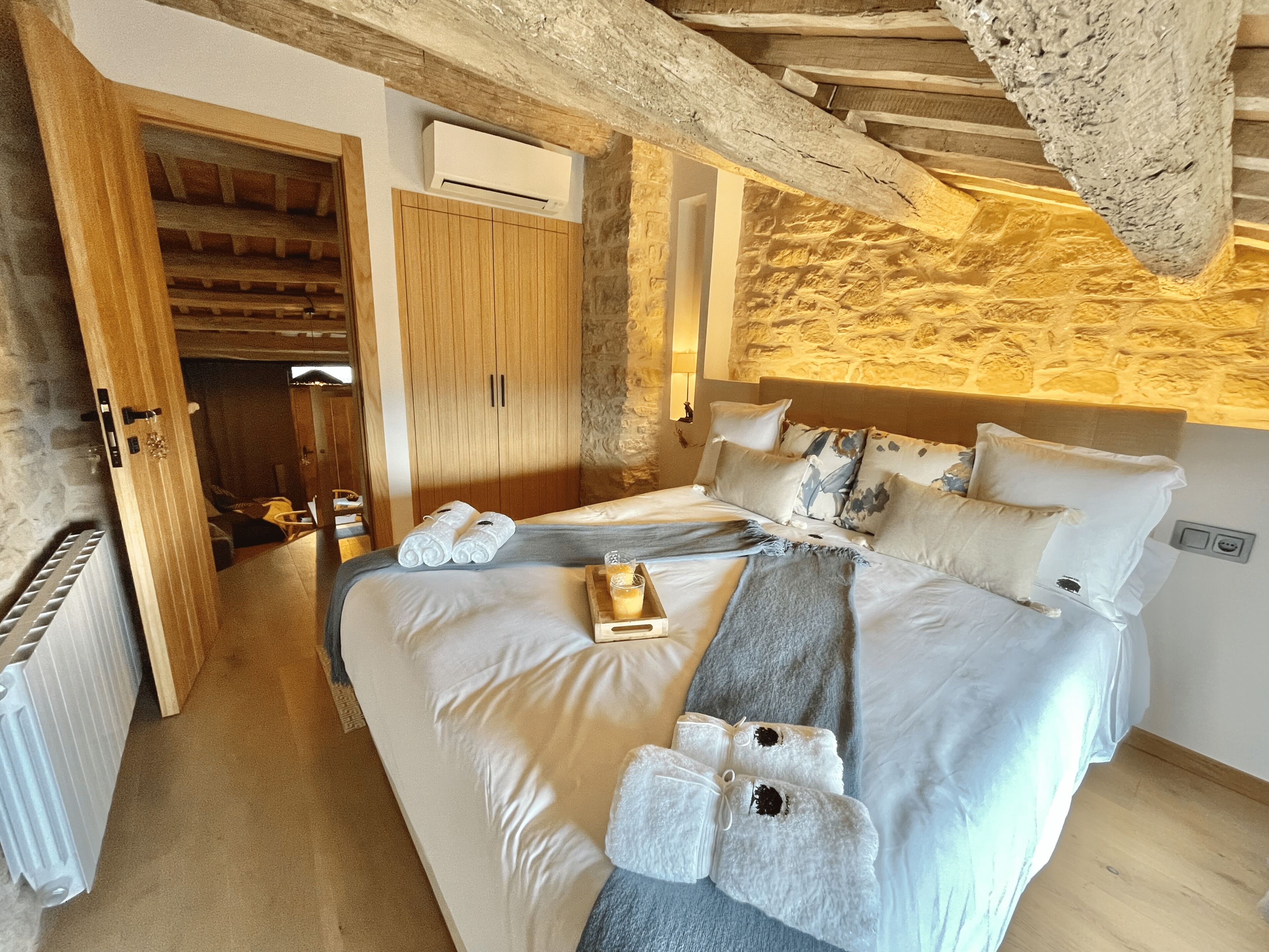 A bedroom with a large bed, wooden wardrobe, and a stone wall.