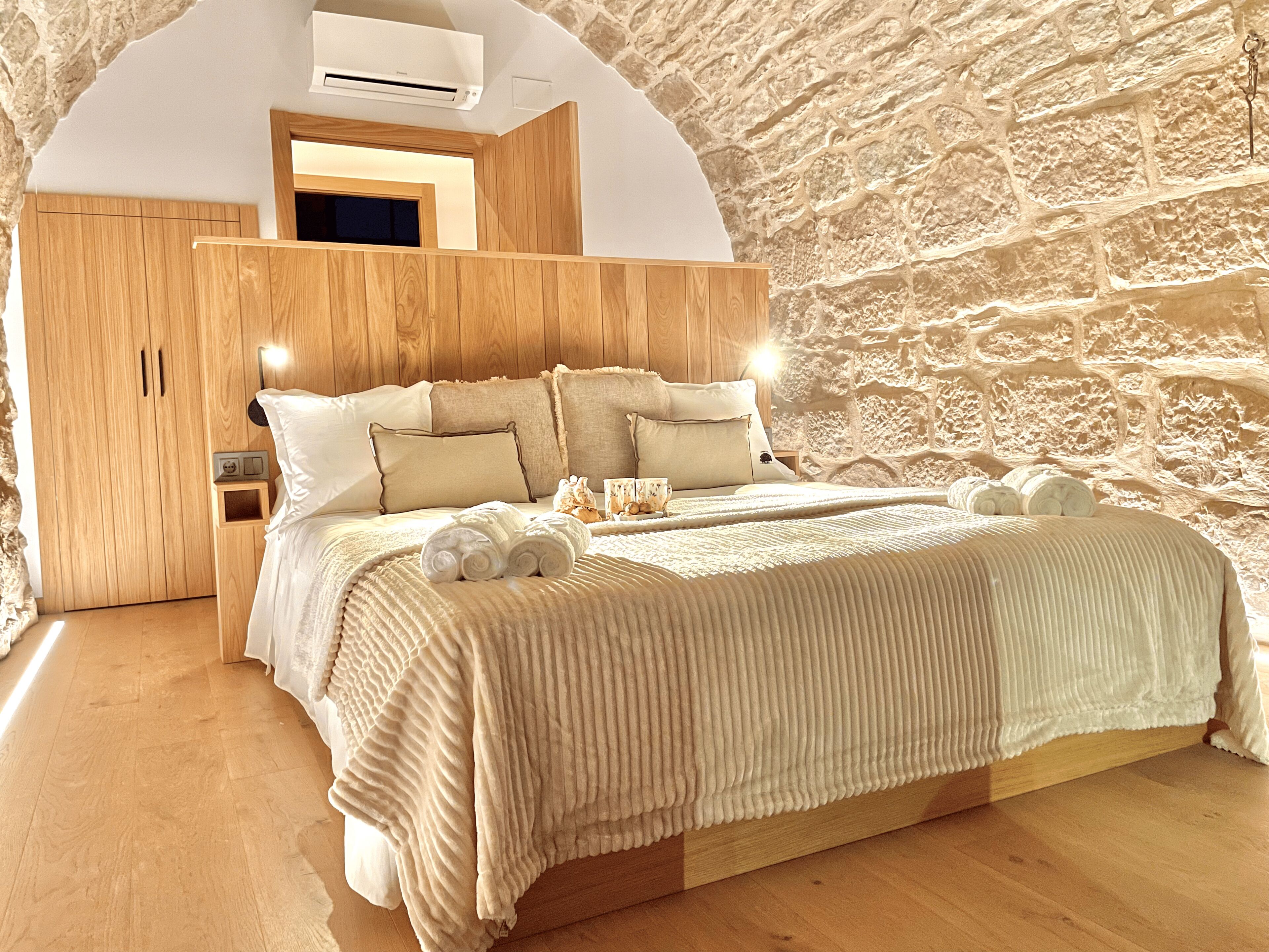 A bedroom with a stone wall, wooden bed frame, and a built-in wardrobe.