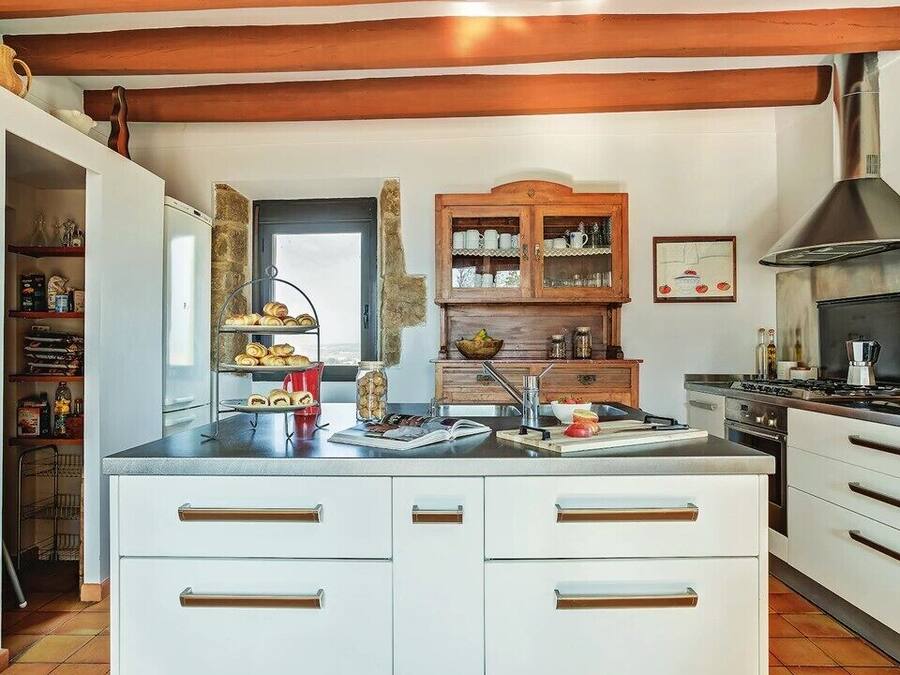 Una cocina con armarios blancos, una campana extractora de acero inoxidable y un mueble de madera con vajilla.
