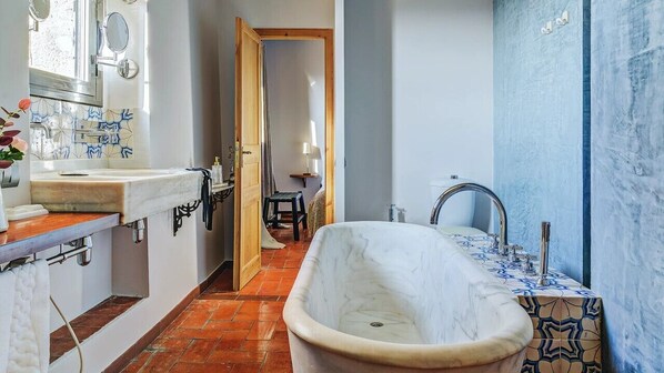 A bathroom with a large bathtub, a sink with a patterned tile backsplash, and a shower area.
