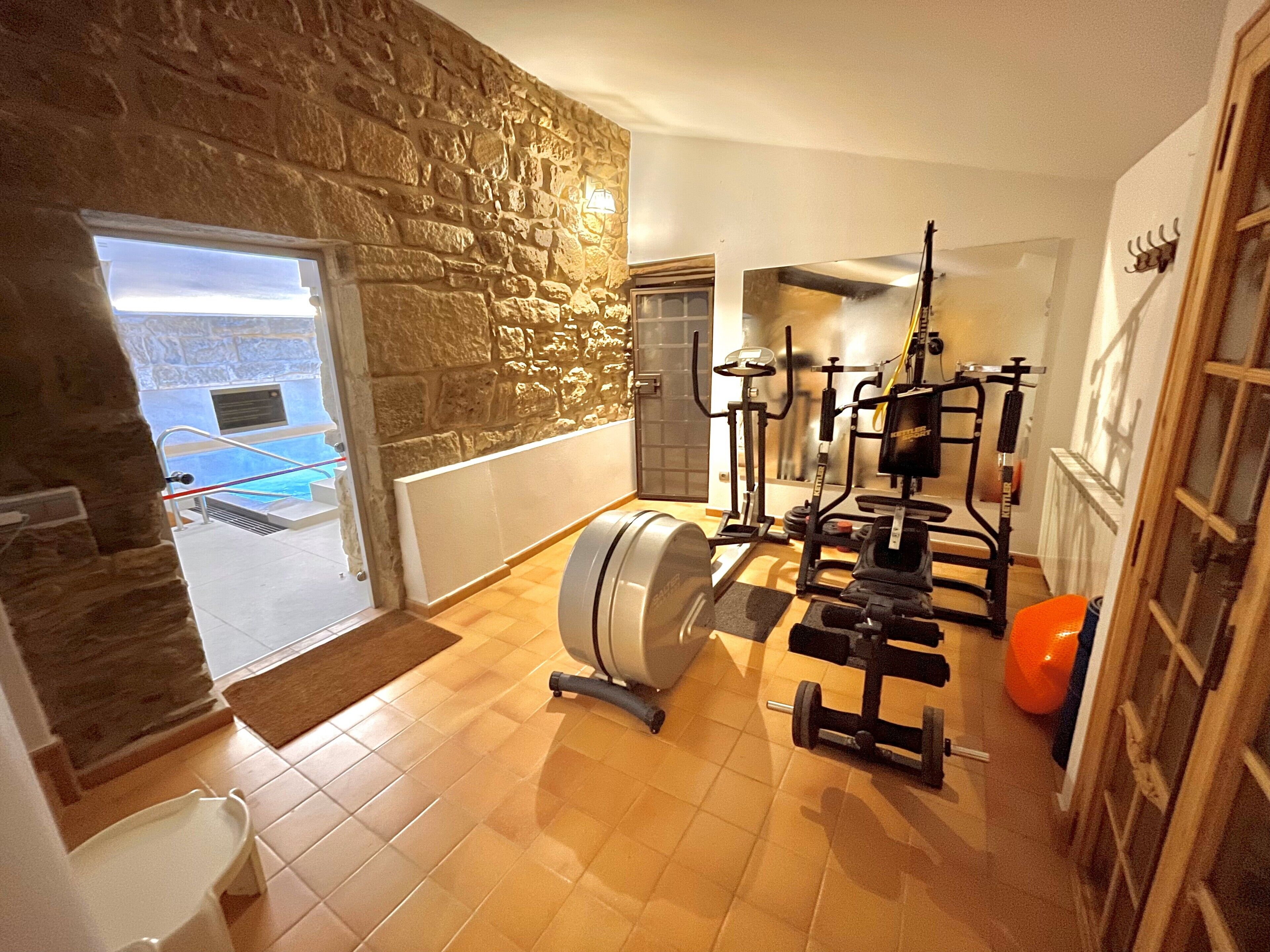 Un gimnasio en casa con equipo de ejercicio, una pared de piedra y vista a una piscina.