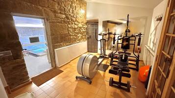 Un gimnasio en casa con equipo de ejercicio, una pared de piedra y vista a una piscina.