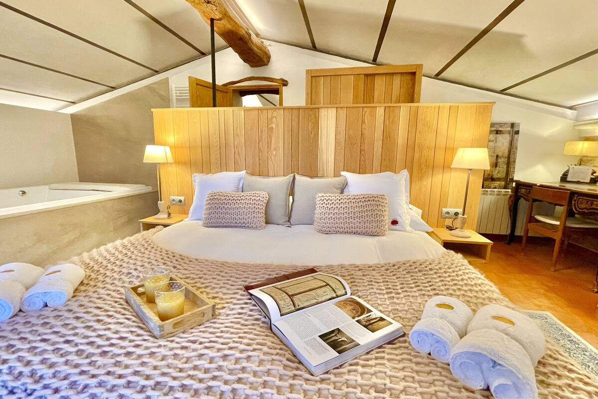 Habitación de hotel con una cama grande, cabecero de madera, lámparas de noche, un escritorio y una bañera.