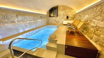 A spa area with a stone wall, a hot tub, wooden loungers, and a small table with a basket.