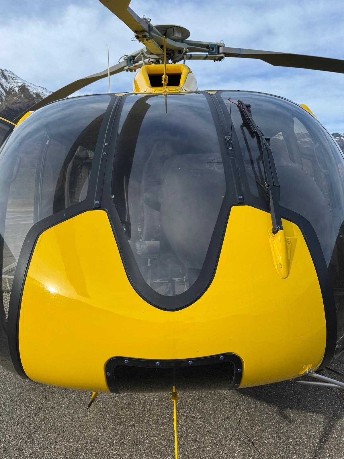 Un helicóptero amarillo y negro con una cabina transparente, estacionado sobre una superficie de hormigón.