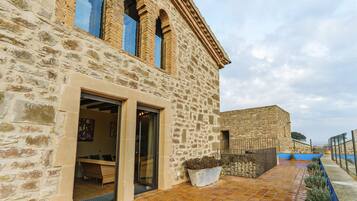 Un edificio de piedra con un patio empedrado, una jardinera grande y un escaparate de vidrio que da a un espacio interior.