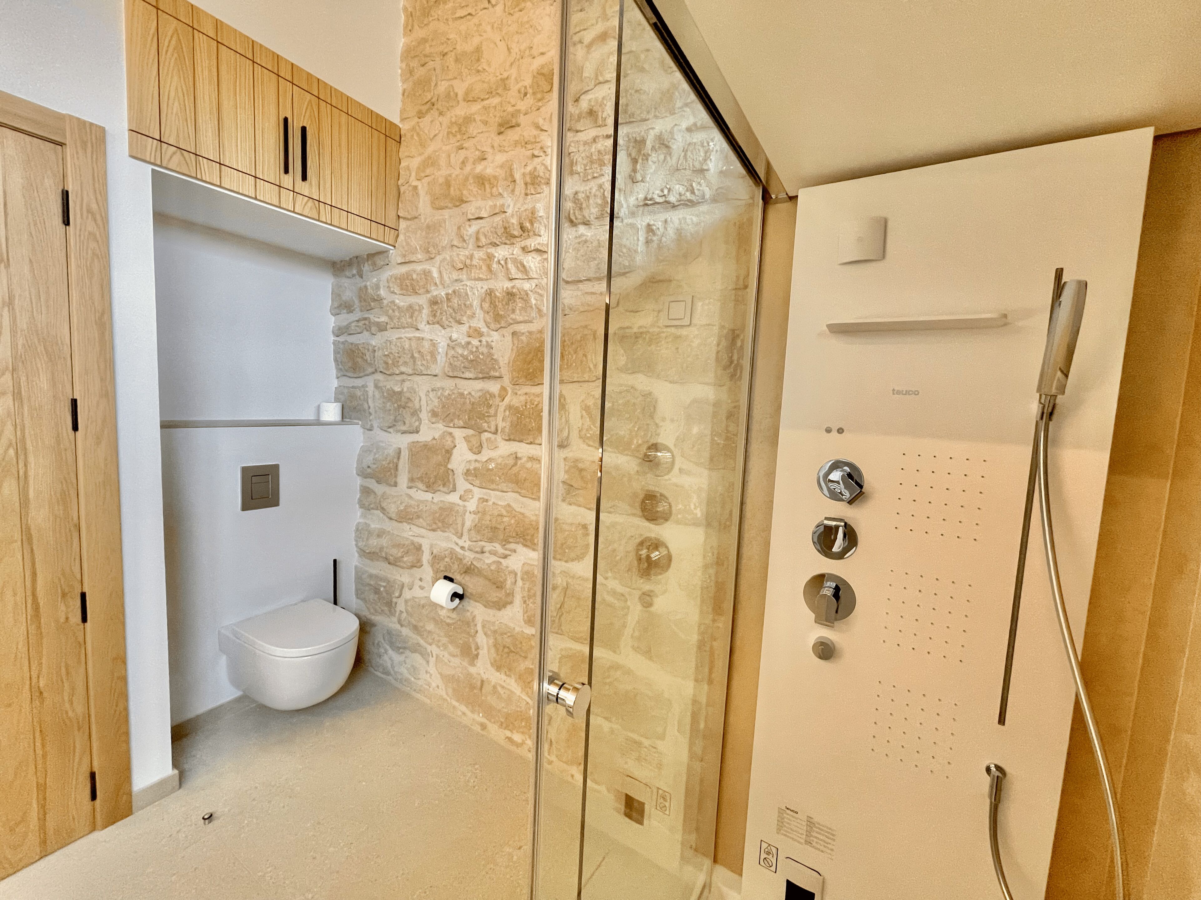 Un baño con pared de piedra, inodoro y ducha con panel de control.