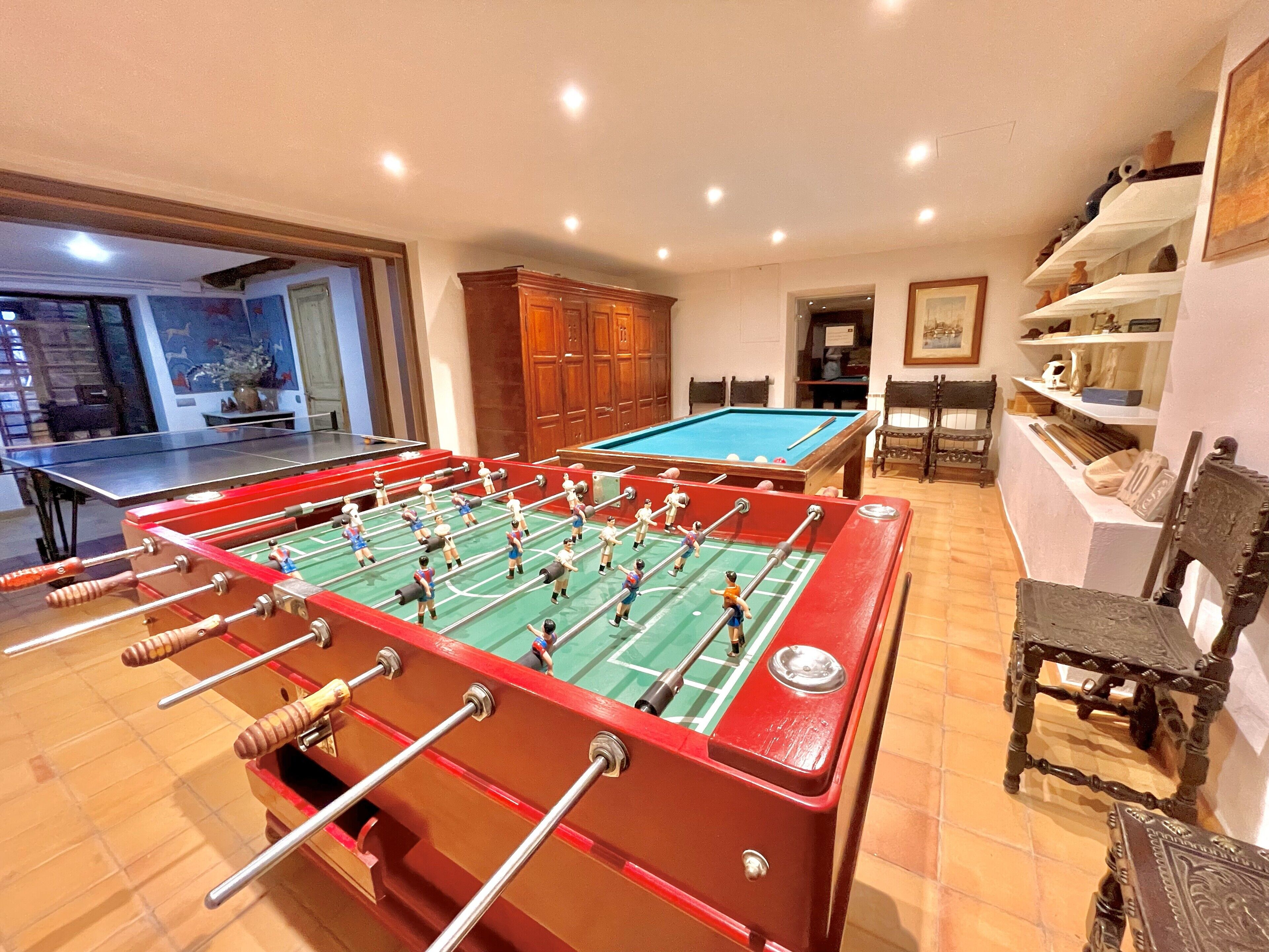 A room with a foosball table, a pool table, wooden cabinets, and a billiards table.