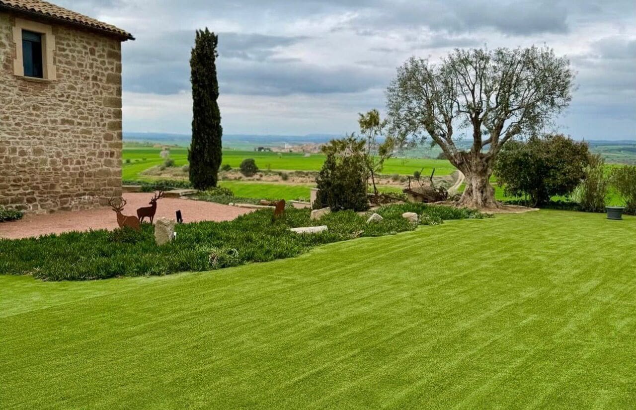 Un edificio de piedra con un césped cuidado, un árbol grande y vistas al campo.