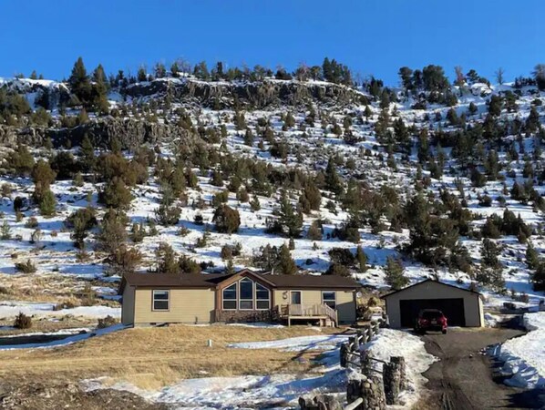 A house with a garage, surrounded by snow-covered ground and trees.