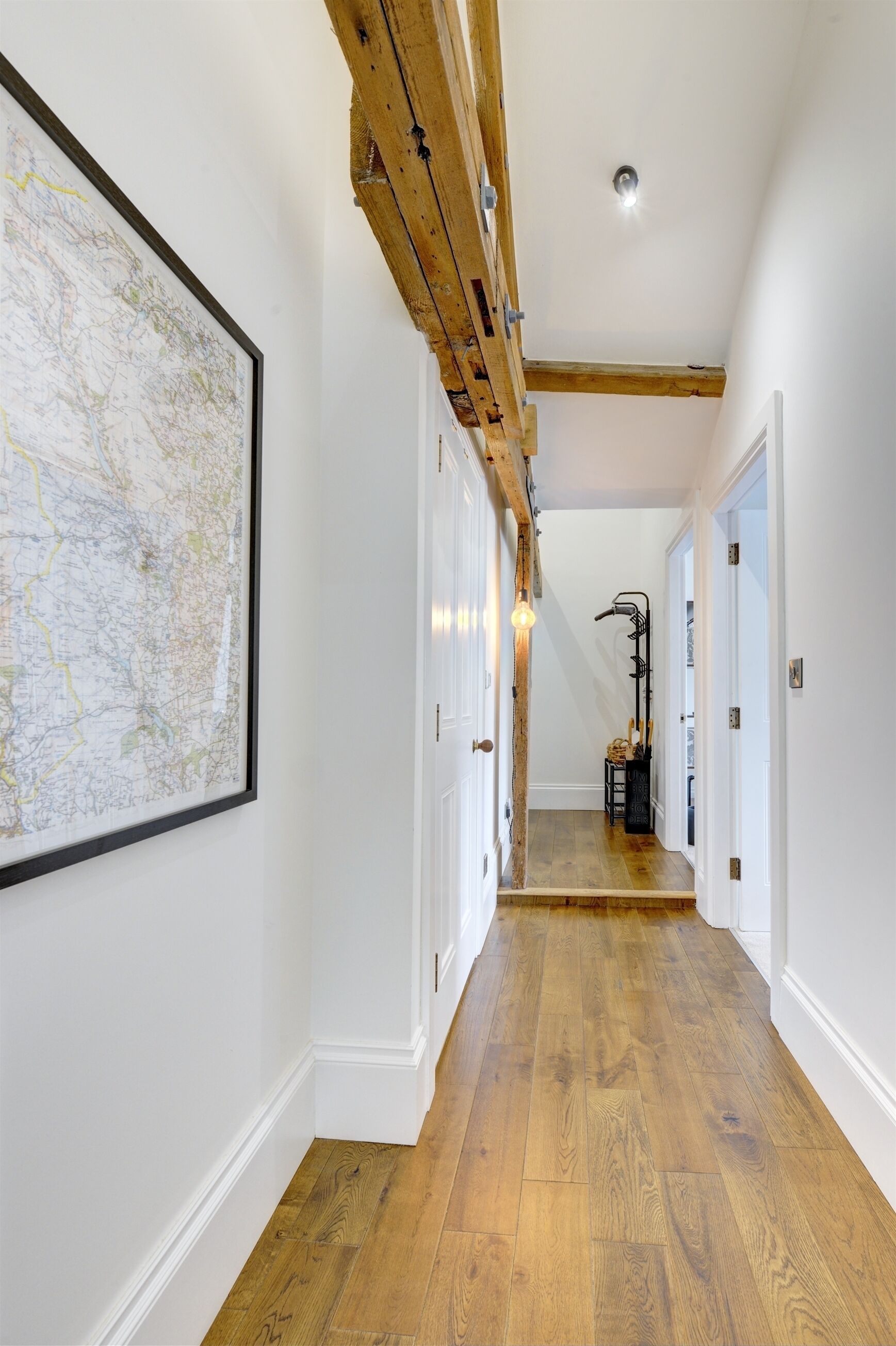 Un couloir doté d’un plancher en bois, de murs blancs et d’une grande carte accrochée au mur de gauche.