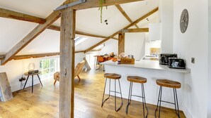 A kitchen with wooden beams, a white countertop, bar stools, and a hanging plant.