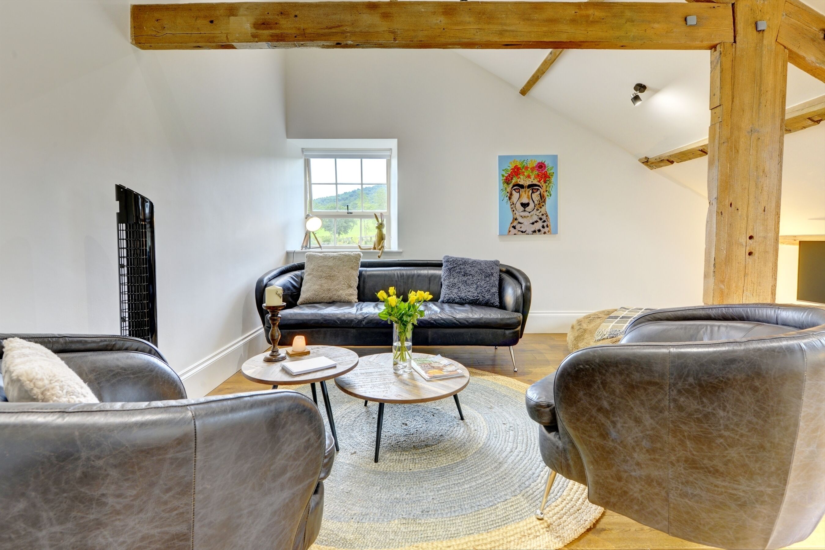 Un salon avec un canapé en cuir noir, deux fauteuils, une table basse et un tableau accroché au mur.