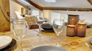 A dining table set with wine glasses, plates, and patterned candle holders in a room with wooden beams and a high ceiling.