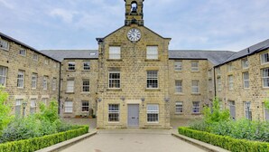 A historic stone building with a central clock tower, symmetrical windows, and a paved courtyard.