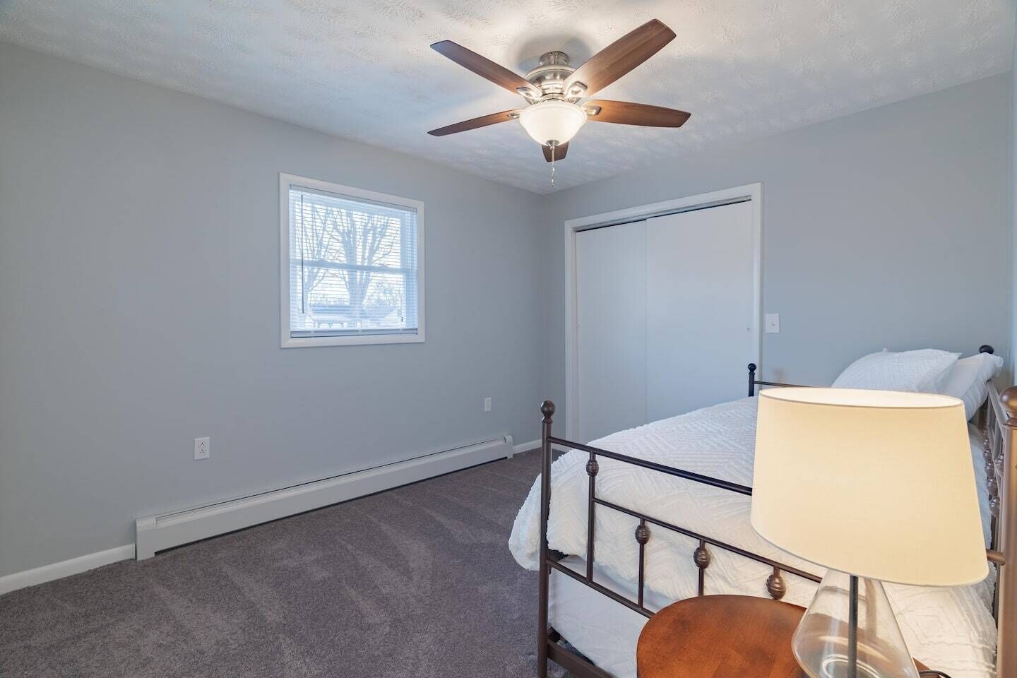 A bedroom with a single bed, a ceiling fan, a window, and a door.