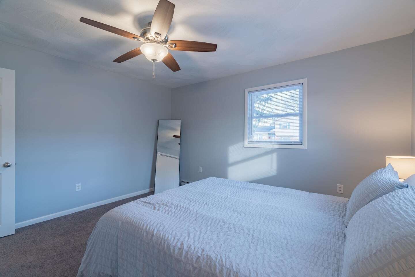 A bedroom with a bed, a ceiling fan, a window, and a mirror.