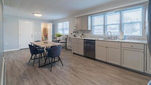 Ett modernt kök med matplats, med ljusa trägolv, vita köksluckor och ett stort fönster som släpper in naturligt ljus.