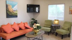 Un salon comprenant un canapé, deux fauteuils, une table basse, un téléviseur et une affiche accrochée au mur.