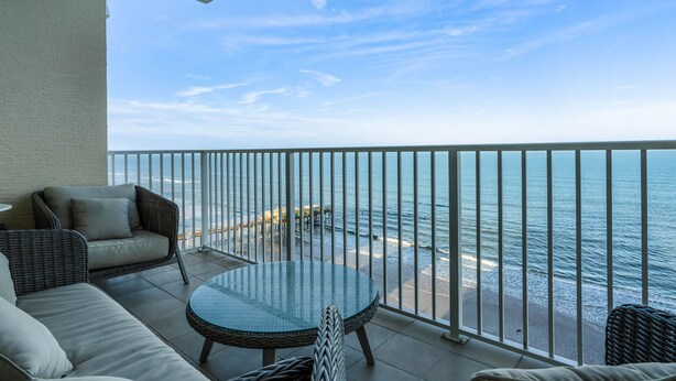 A balcony with wicker furniture, a glass table, and a view of the ocean. - Professionally Designed & Decorated Luxury Oceanfront Paradise (Daytona Beach)