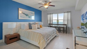 A bedroom with a bed, a desk, and a window with a view. - Professionally Designed & Decorated Luxury Oceanfront Paradise (Daytona Beach)