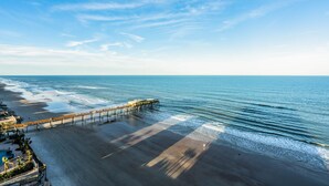 A beach with a pier extending into the ocean, a sandy beach, and a clear sky. - Professionally Designed & Decorated Luxury Oceanfront Paradise (Daytona Beach)