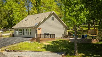 A small, single-story building with a sloped roof, a front porch with a bench, and a gravel driveway.