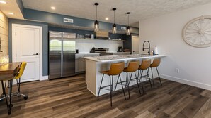 Une cuisine moderne avec un îlot central, des tabourets de bar et une grande horloge au mur.